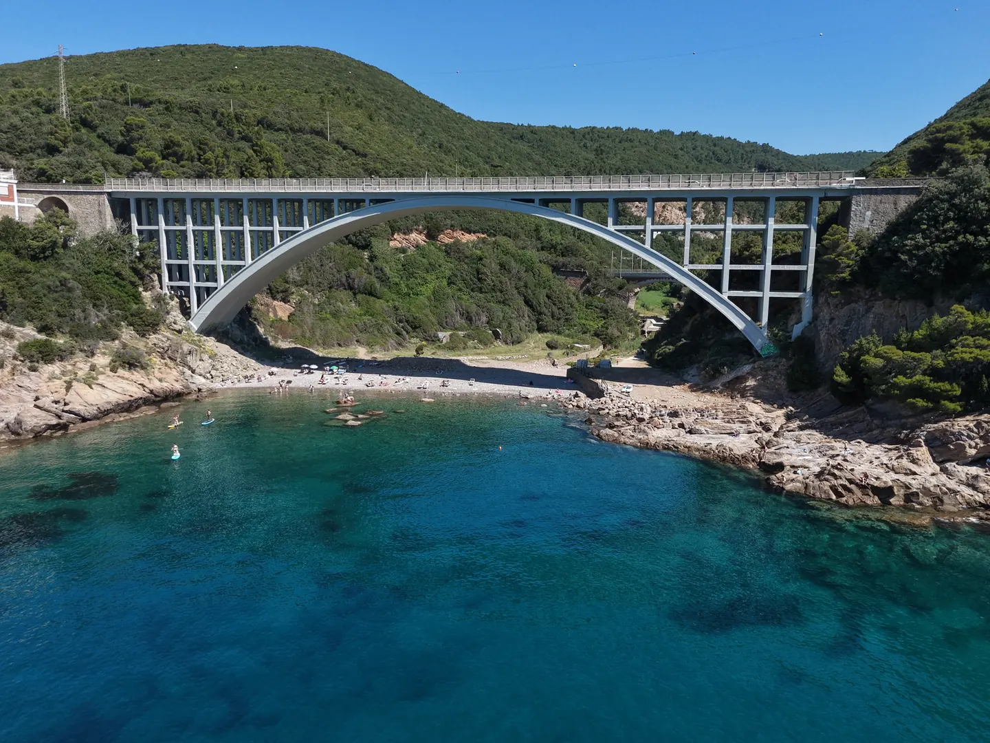 Ponte di Calafuria: l'arco sull'insenatura con bagnanti e acqua turchese, ripresa aerea con drone, Livorno