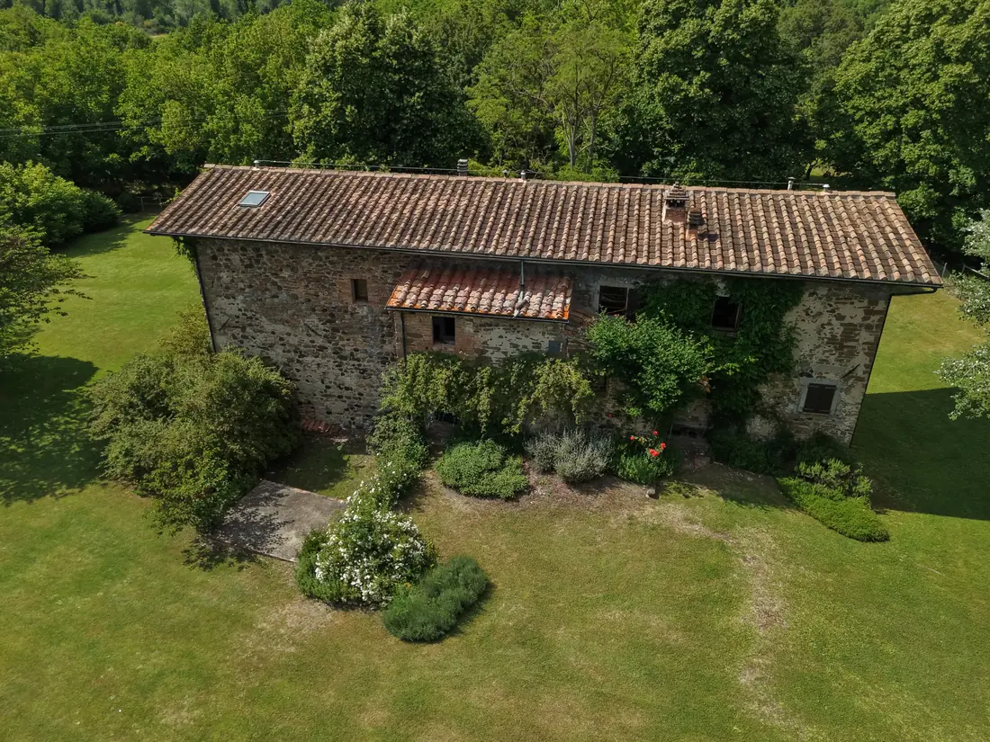 Facciata di casale toscano in pietra con giardino, ripresa aerea ravvicinata