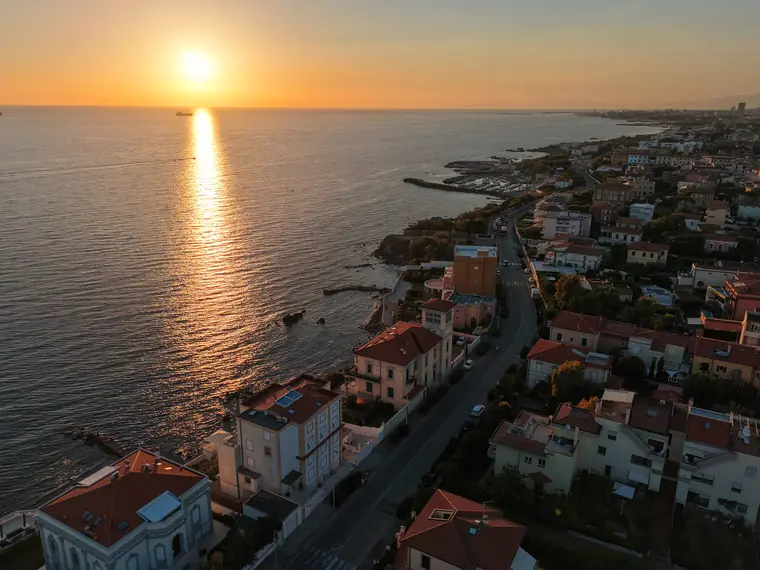 Tramonto con scia di sole sull'acqua e scogli, foto aerea