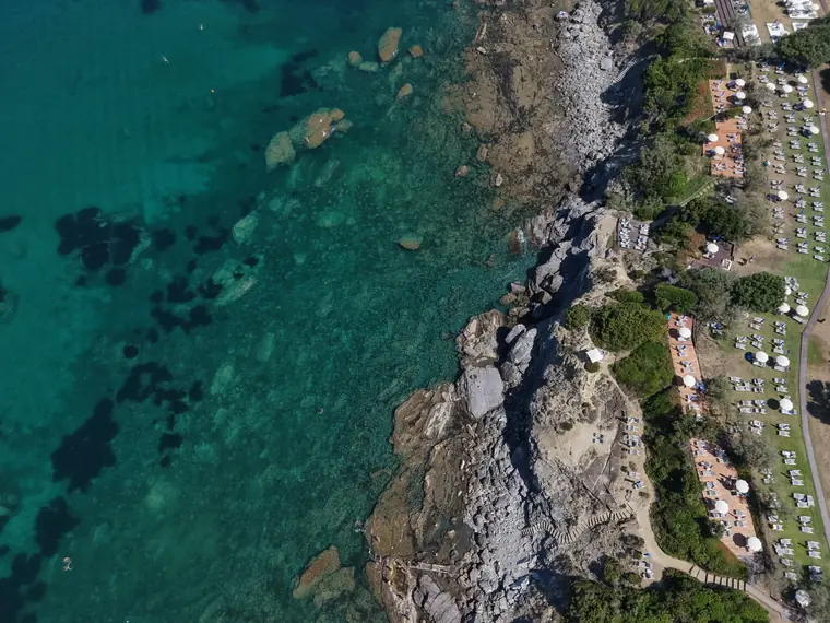 Scogliera con ombrelloni e scale a mare viste in verticale dal drone